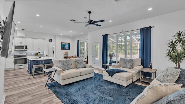 living room featuring ceiling fan, sink, light hardwood / wood-style floors, and a textured ceiling