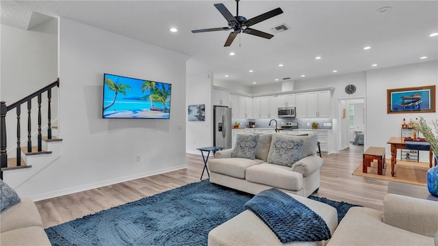 living room featuring ceiling fan, sink, and light wood-type flooring