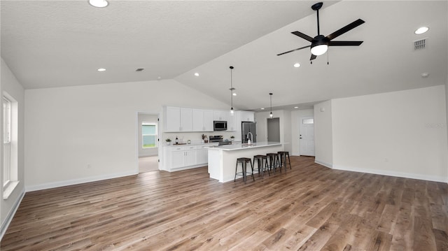 kitchen featuring white cabinets, an island with sink, decorative light fixtures, a kitchen bar, and stainless steel appliances