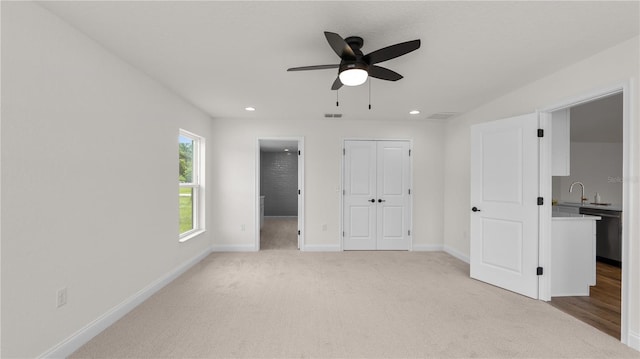 unfurnished bedroom featuring light carpet, ensuite bathroom, ceiling fan, and sink