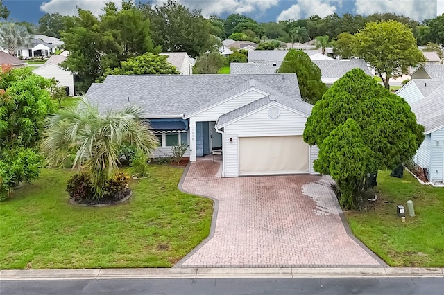 view of front facade featuring an attached garage, roof with shingles, decorative driveway, a residential view, and a front lawn