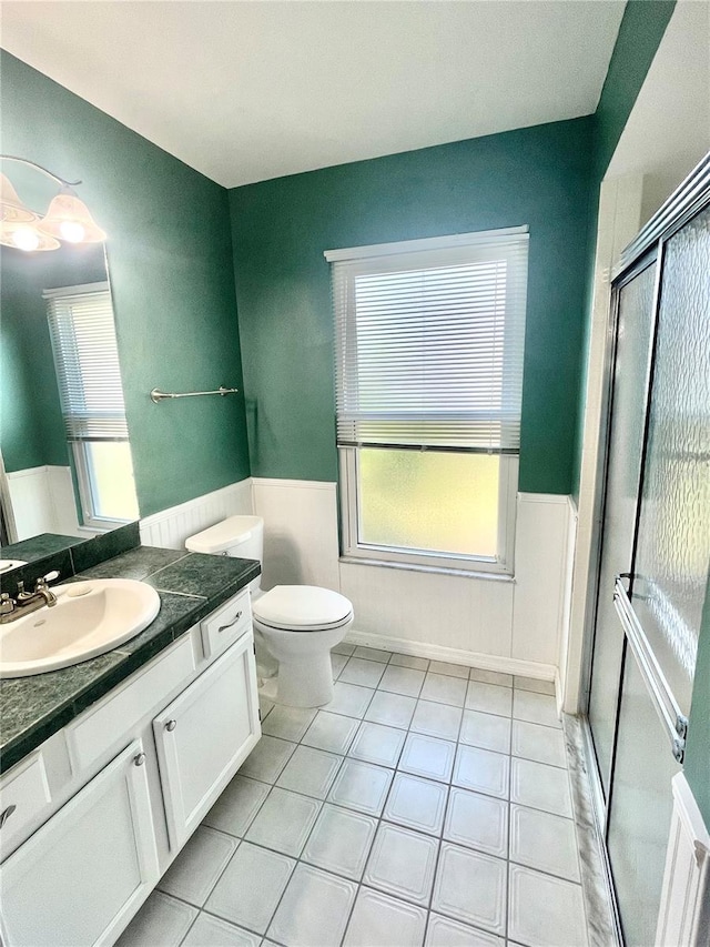 bathroom featuring toilet, a wainscoted wall, tile patterned floors, vanity, and a healthy amount of sunlight