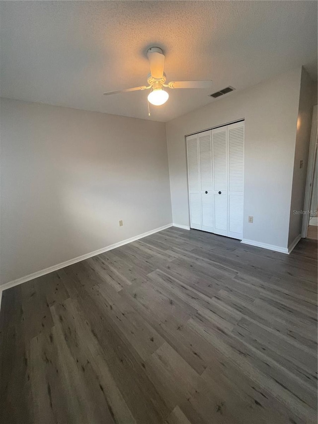 unfurnished bedroom featuring a textured ceiling, dark wood-type flooring, visible vents, baseboards, and a closet