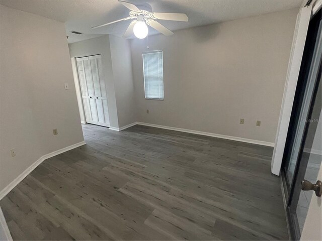 empty room with ceiling fan, dark wood finished floors, and baseboards