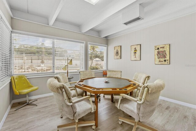 dining room with beam ceiling, wood walls, and light hardwood / wood-style floors