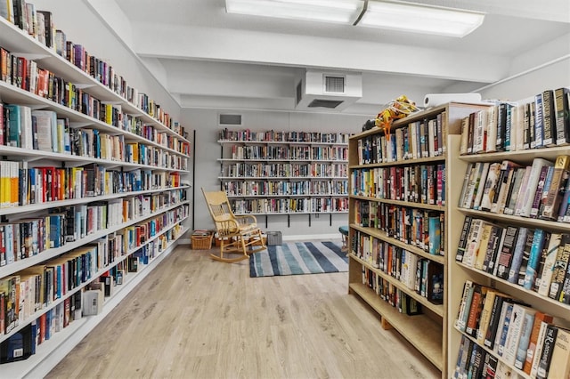 living area with beam ceiling, bookshelves, and wood finished floors