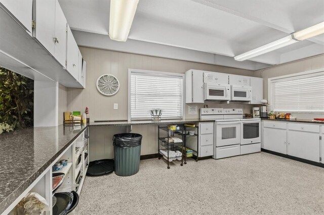 kitchen with white cabinetry, dark stone counters, and white appliances