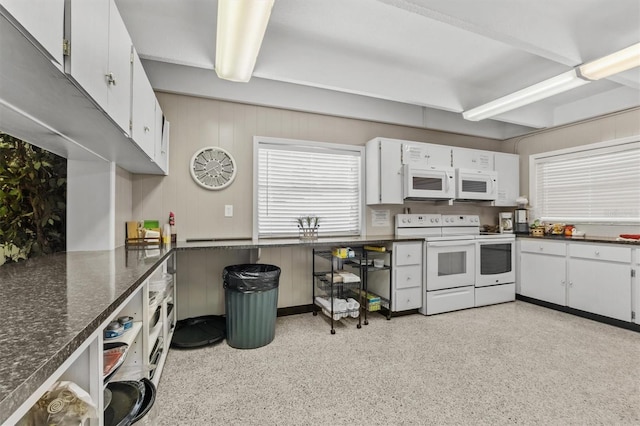 kitchen with dark countertops, white cabinetry, and white appliances