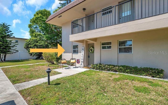 view of exterior entry with board and batten siding, fence, a balcony, a yard, and stucco siding