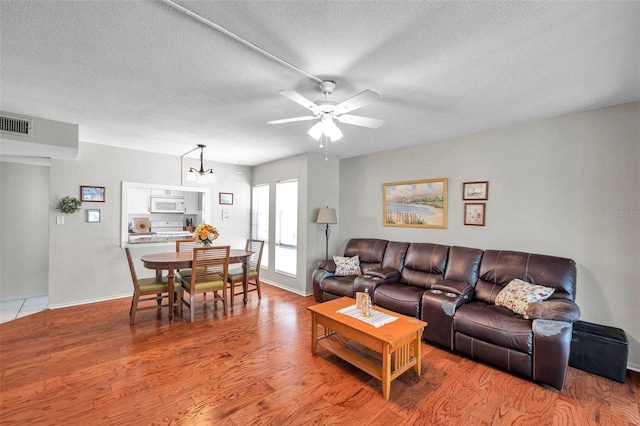 living room featuring a textured ceiling, ceiling fan with notable chandelier, baseboards, wood finished floors, and visible vents