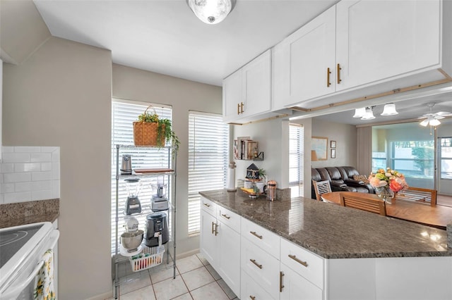 kitchen featuring white cabinets, a peninsula, light tile patterned floors, and dark stone countertops