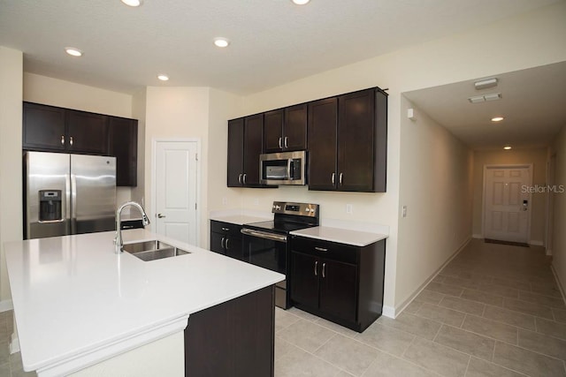 kitchen featuring dark brown cabinetry, stainless steel appliances, sink, light tile patterned floors, and an island with sink