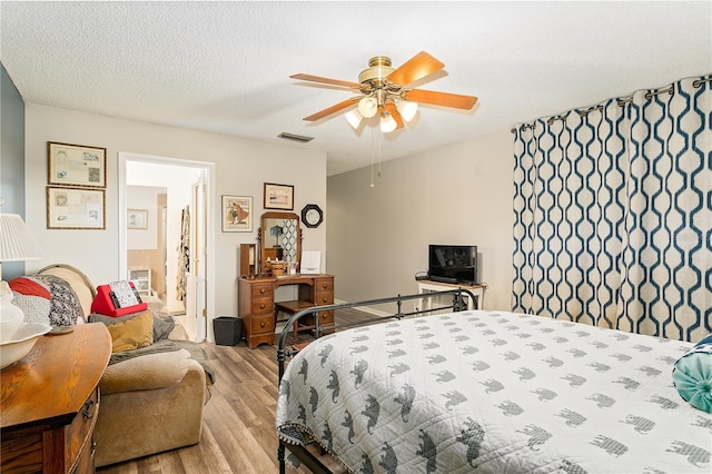 bedroom with a textured ceiling, light hardwood / wood-style flooring, ceiling fan, and connected bathroom