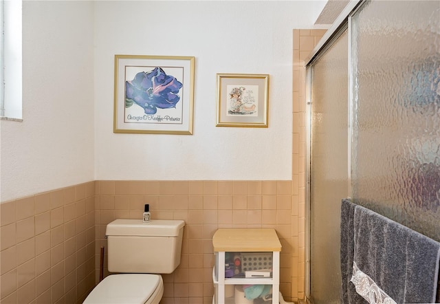 bathroom with a shower with door, tile walls, and toilet