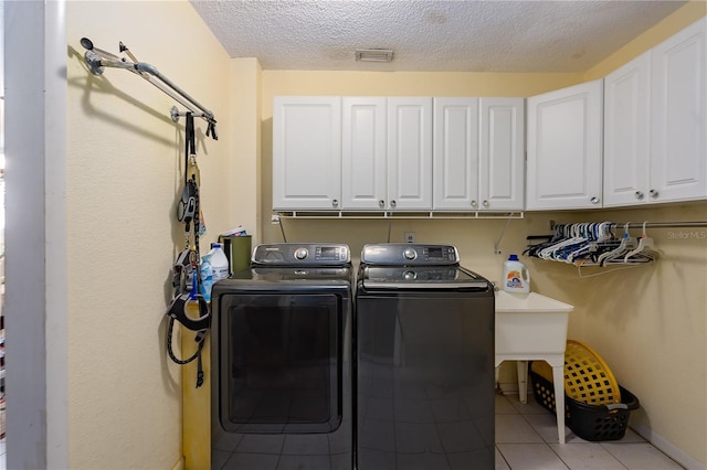 washroom with cabinets, independent washer and dryer, a textured ceiling, and light tile patterned floors