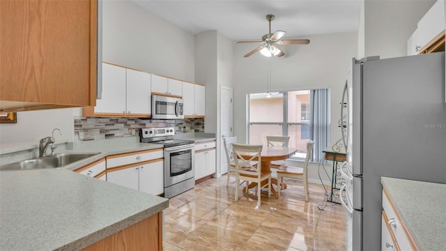 kitchen featuring ceiling fan, sink, a high ceiling, white cabinets, and appliances with stainless steel finishes