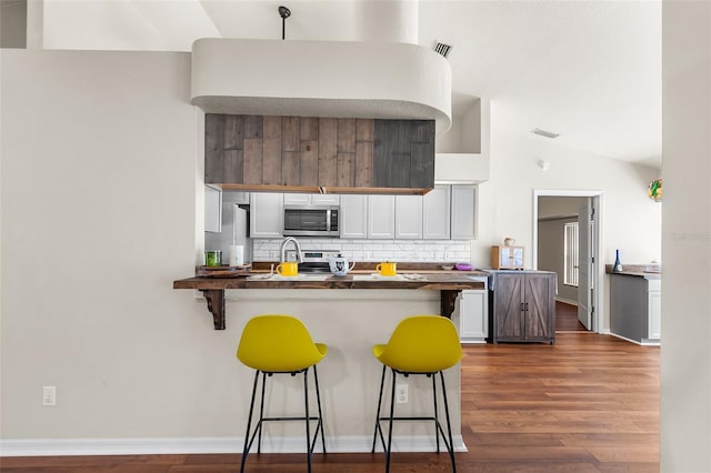 kitchen featuring a breakfast bar area, dark wood finished floors, white cabinetry, appliances with stainless steel finishes, and tasteful backsplash