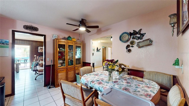 tiled dining space with ceiling fan and wooden walls