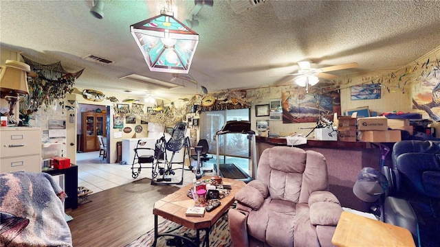 living room featuring ceiling fan, light wood-type flooring, and a textured ceiling