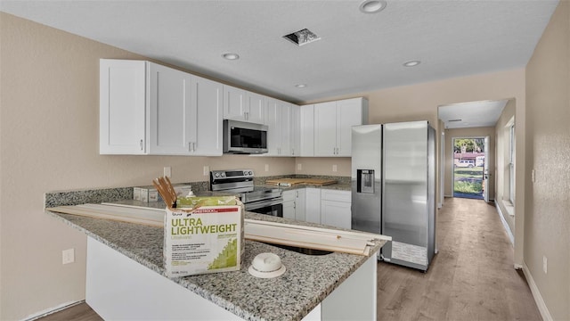 kitchen featuring white cabinetry, appliances with stainless steel finishes, kitchen peninsula, and light stone counters