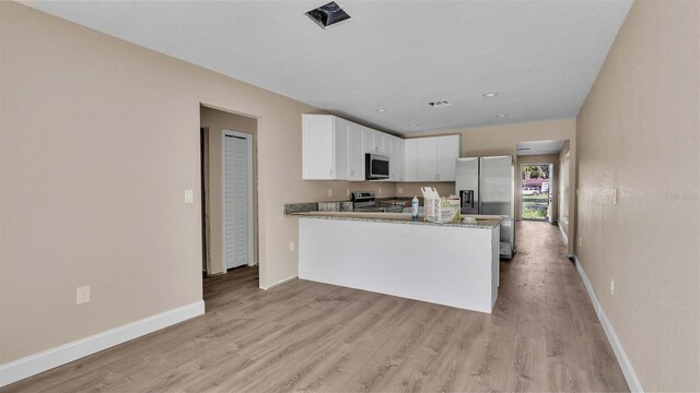 kitchen featuring appliances with stainless steel finishes, light stone countertops, white cabinets, kitchen peninsula, and light wood-type flooring