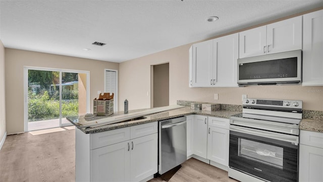 kitchen featuring light stone counters, appliances with stainless steel finishes, kitchen peninsula, and white cabinets