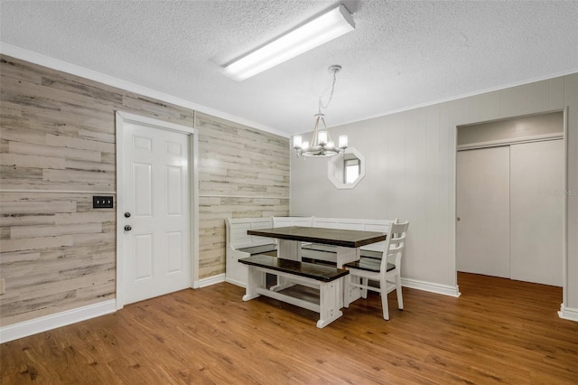 dining room featuring crown molding, a textured ceiling, hardwood / wood-style flooring, and wood walls