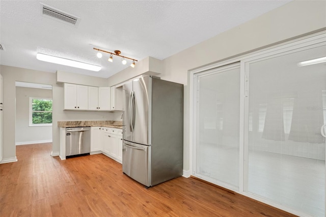 kitchen featuring a textured ceiling, stainless steel appliances, white cabinets, and light hardwood / wood-style floors