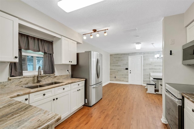 kitchen with white cabinetry, a textured ceiling, stainless steel appliances, sink, and light hardwood / wood-style floors