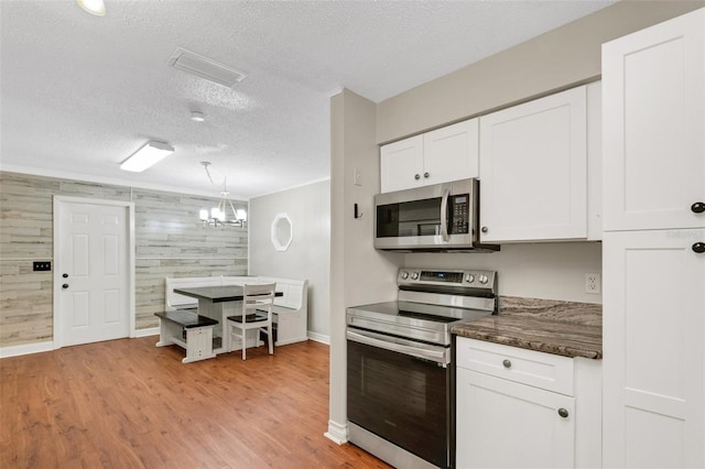 kitchen featuring wooden walls, decorative light fixtures, light wood-type flooring, appliances with stainless steel finishes, and a textured ceiling