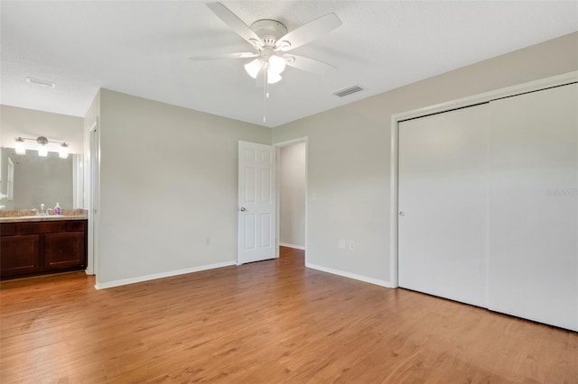 unfurnished bedroom with ensuite bath, light wood-type flooring, sink, a closet, and ceiling fan