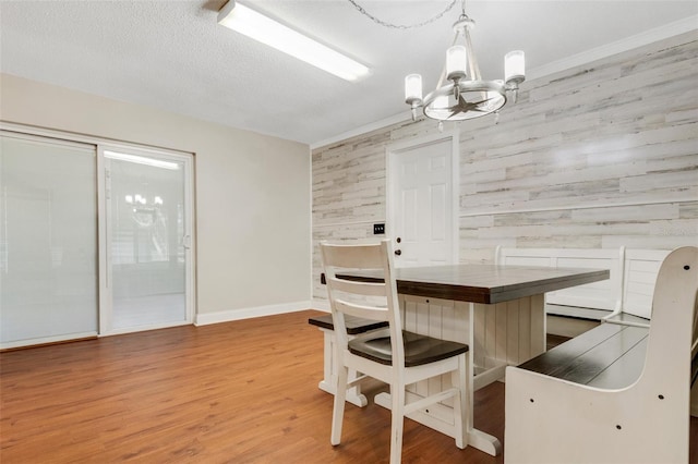 dining room with crown molding, a textured ceiling, a chandelier, wood walls, and hardwood / wood-style flooring