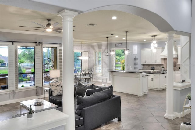 tiled living room featuring ceiling fan with notable chandelier, plenty of natural light, crown molding, and sink