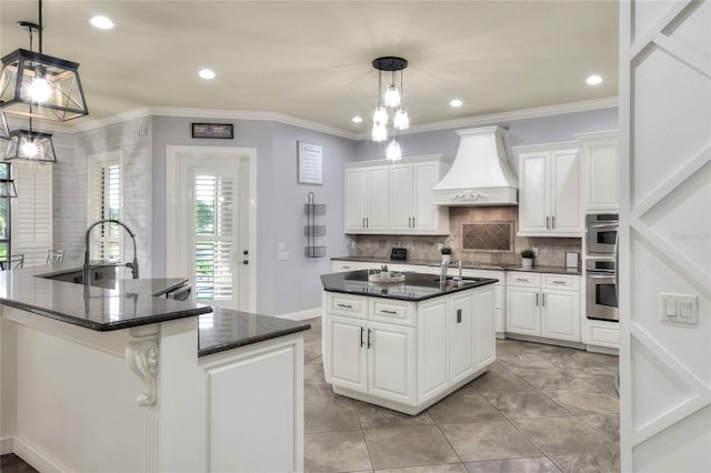 kitchen with white cabinetry, custom range hood, and an island with sink