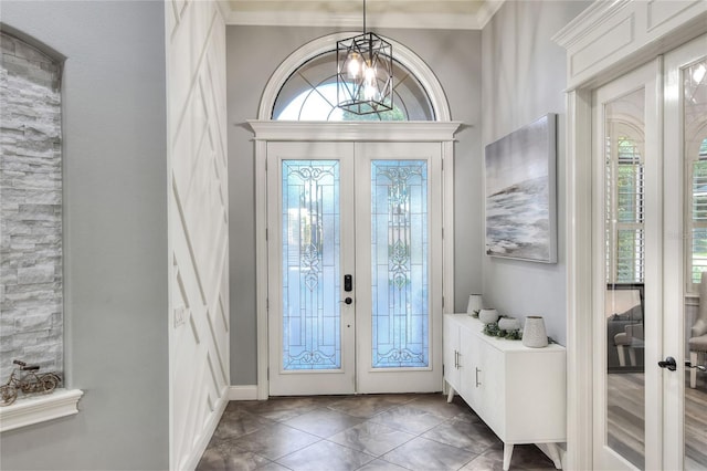 tiled foyer entrance featuring a wealth of natural light, french doors, crown molding, and a notable chandelier