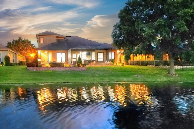 back house at dusk with a lawn and a water view