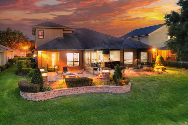 back house at dusk with a fire pit, a yard, and a patio