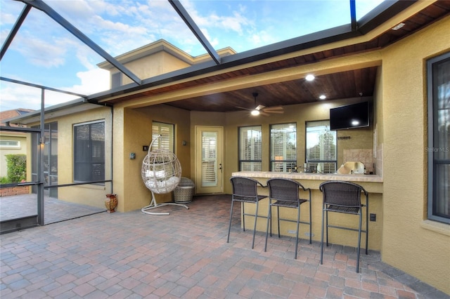 view of patio with glass enclosure, ceiling fan, and exterior bar