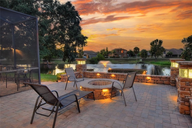 patio terrace at dusk featuring a lanai, a water view, and a fire pit