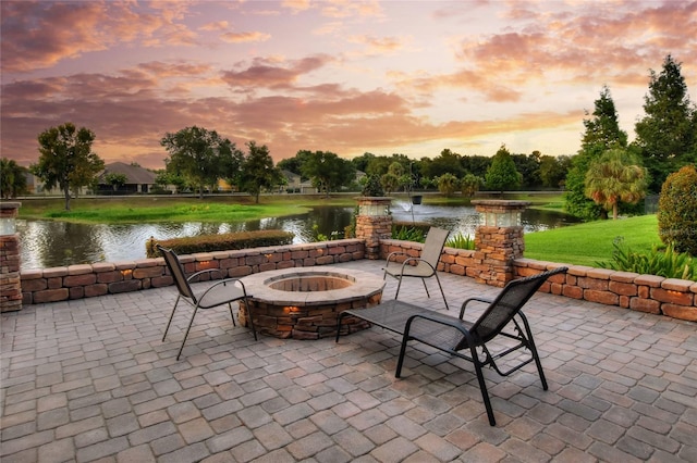 patio terrace at dusk featuring a fire pit and a water view