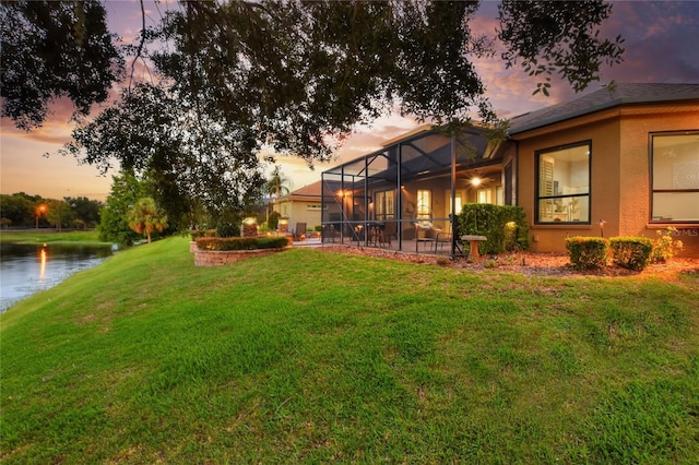 yard at dusk featuring a lanai and a water view