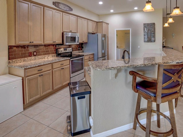 kitchen featuring decorative backsplash, a breakfast bar, stainless steel appliances, pendant lighting, and light brown cabinets