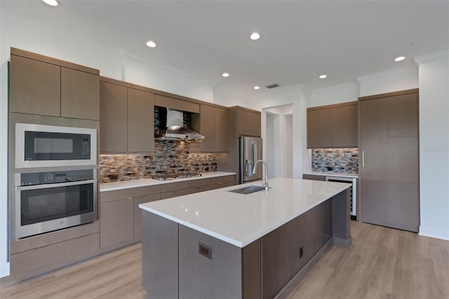 kitchen featuring wall chimney range hood, stainless steel appliances, tasteful backsplash, sink, and a large island