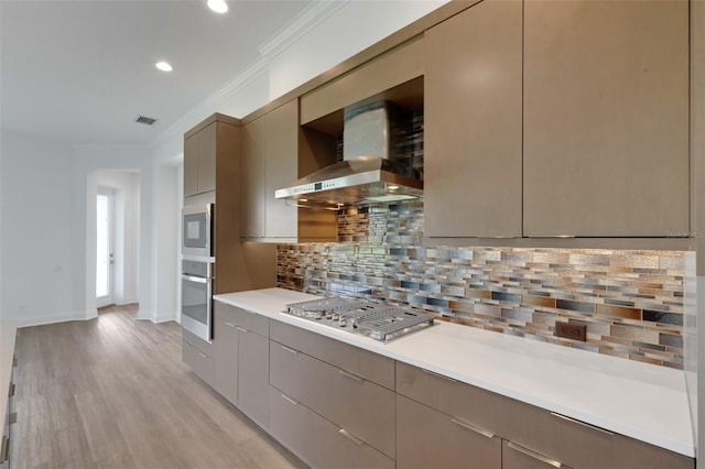 kitchen featuring backsplash, light hardwood / wood-style floors, crown molding, stainless steel gas cooktop, and wall chimney exhaust hood