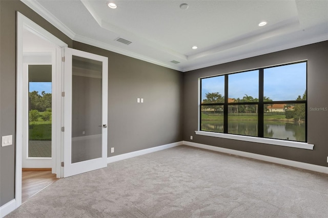 empty room with a raised ceiling, light colored carpet, a water view, and crown molding