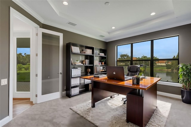 home office featuring a raised ceiling, light colored carpet, a water view, and ornamental molding