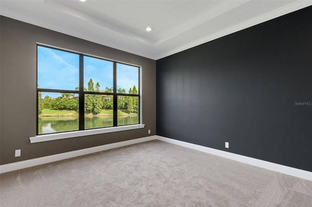 carpeted spare room with ornamental molding, a raised ceiling, and a water view