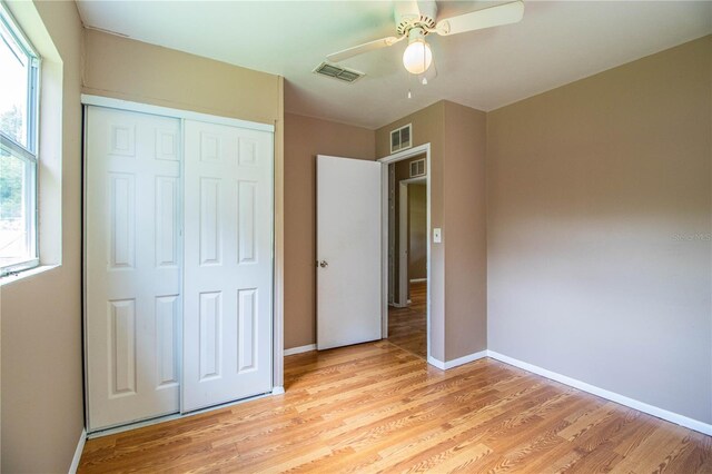 unfurnished bedroom with ceiling fan, light hardwood / wood-style flooring, a closet, and multiple windows