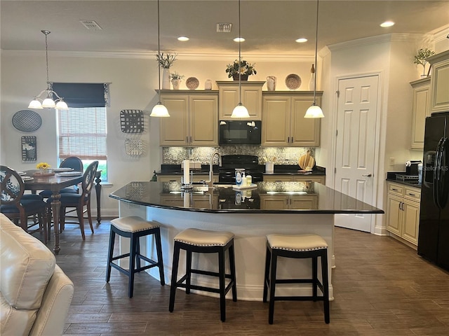 kitchen with dark wood-type flooring, an inviting chandelier, pendant lighting, a kitchen island with sink, and black appliances