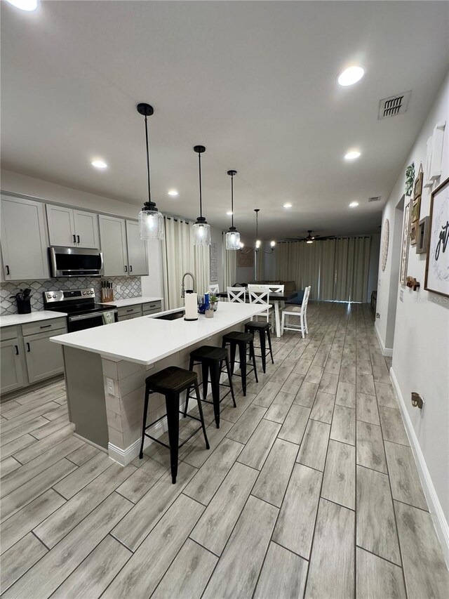 kitchen with sink, a kitchen island with sink, light hardwood / wood-style floors, stainless steel appliances, and gray cabinets